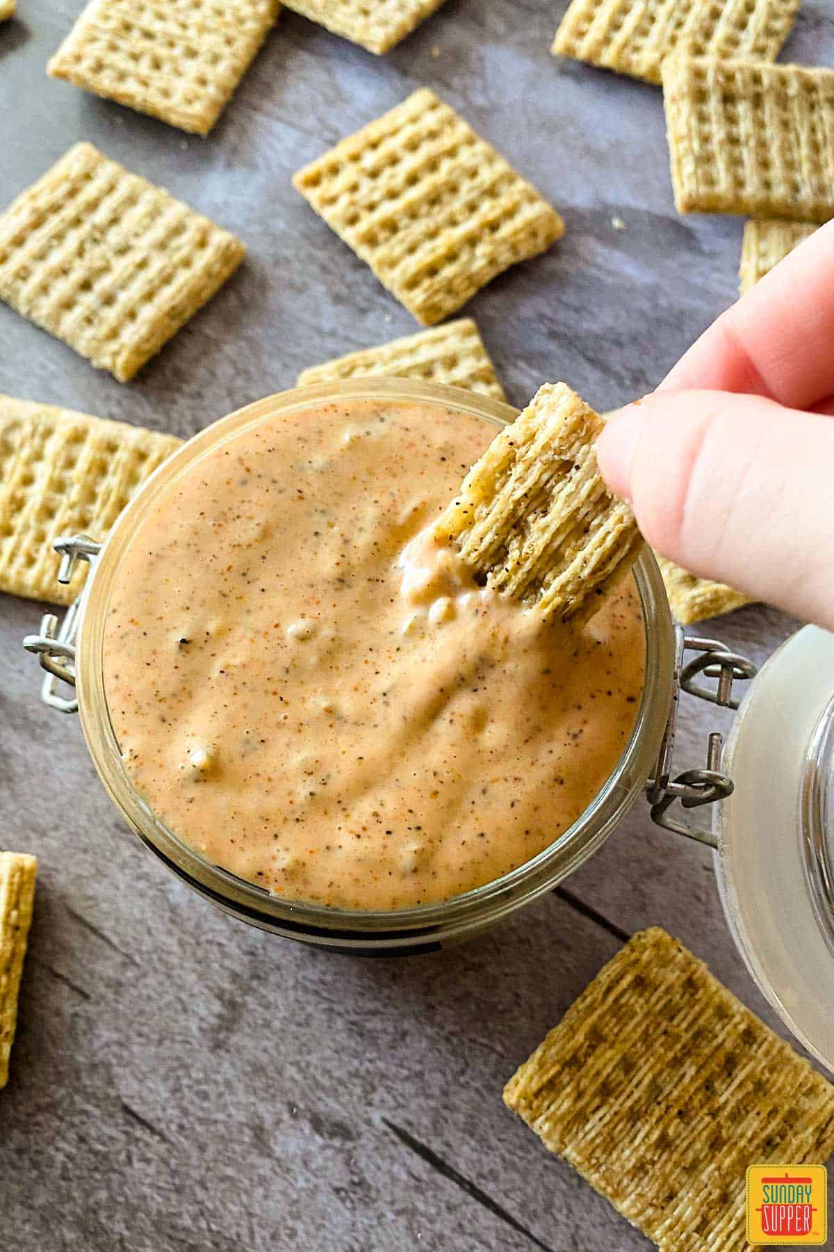 Dipping a cracker into remoulade sauce in a glass jar