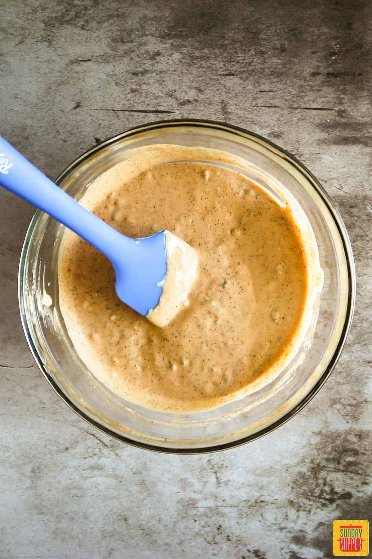 Stirring remoulade sauce in a glass bowl with a blue spatula