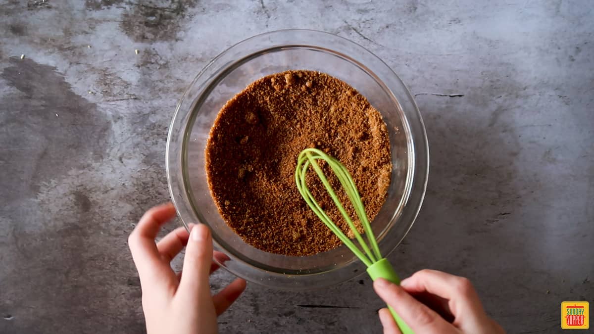 mixing sweet and salty roast beef rub in a glass bowl with a tiny green whisk