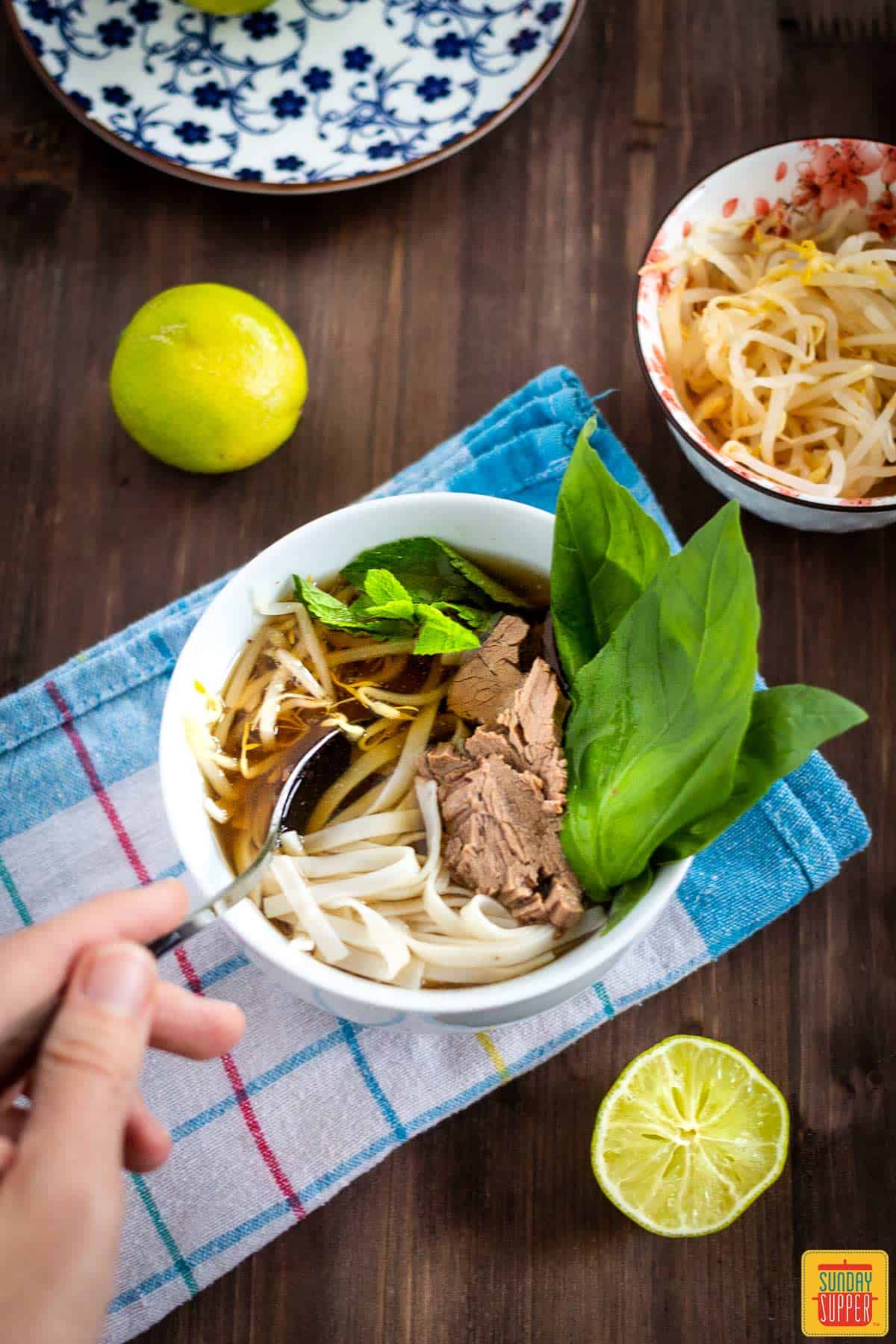 Dipping a spoon into beef pho in a bowl