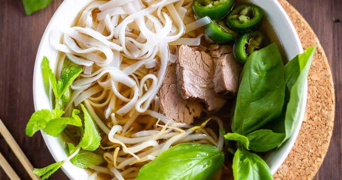 Beef pho in a white bowl with basil and noodles