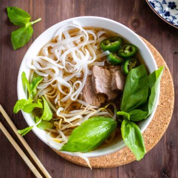 Beef pho in a white bowl with basil and noodles
