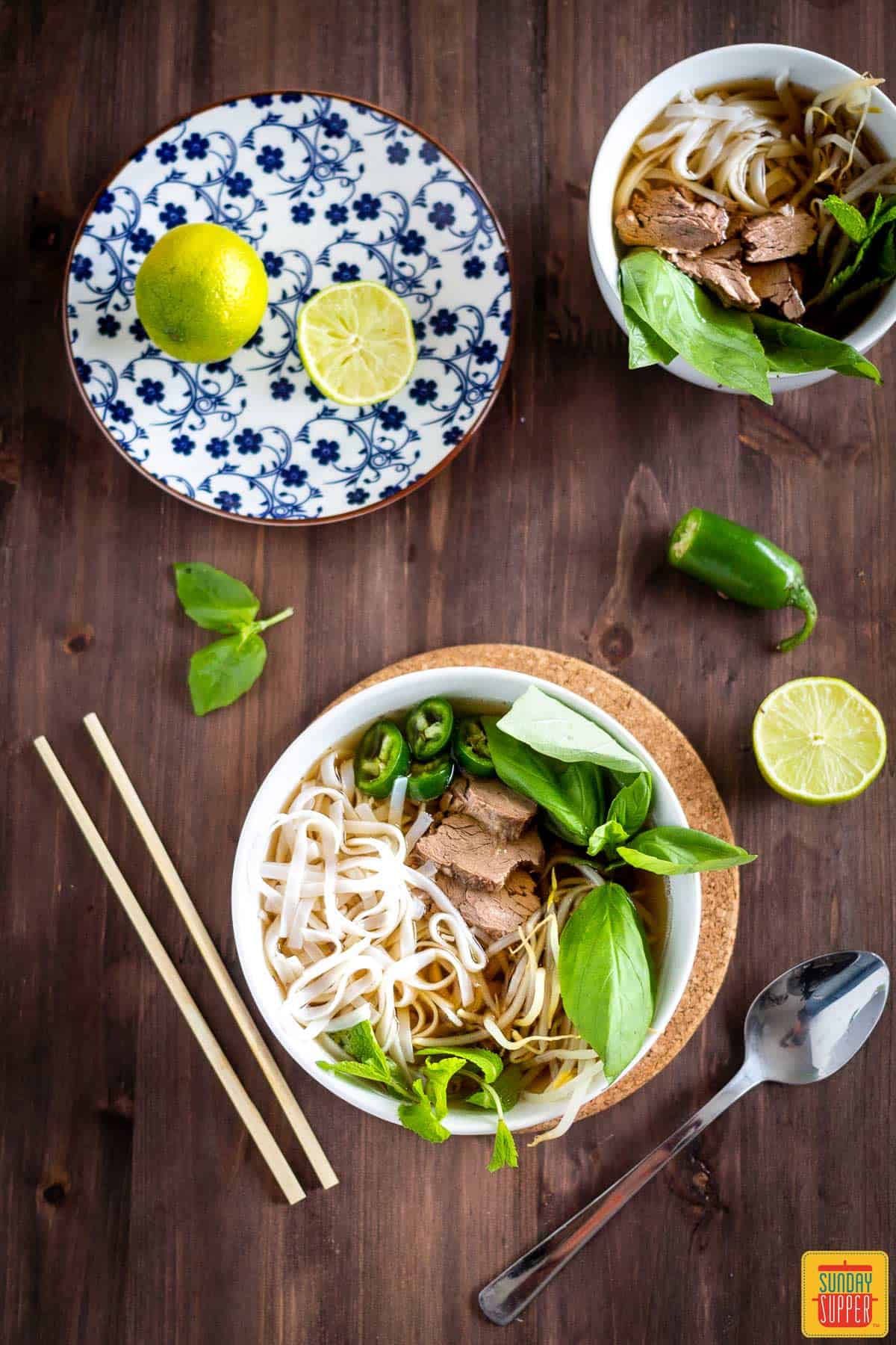 Instant pot pho in two bowls with citrus to the side