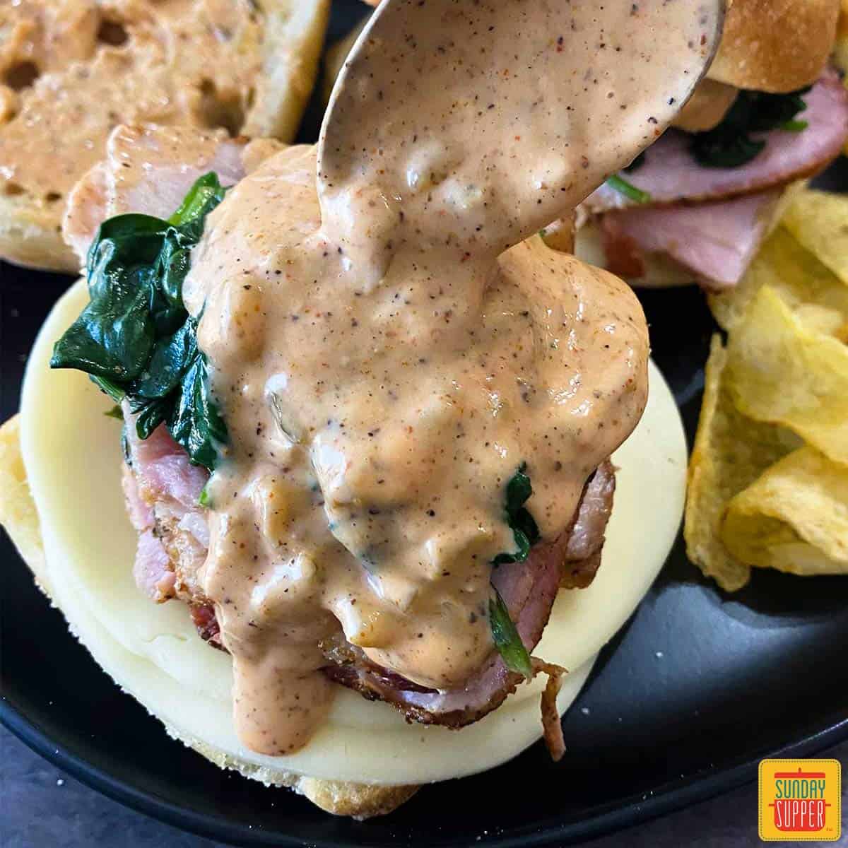 topping a pork sandwich with remoulade sauce on a spoon