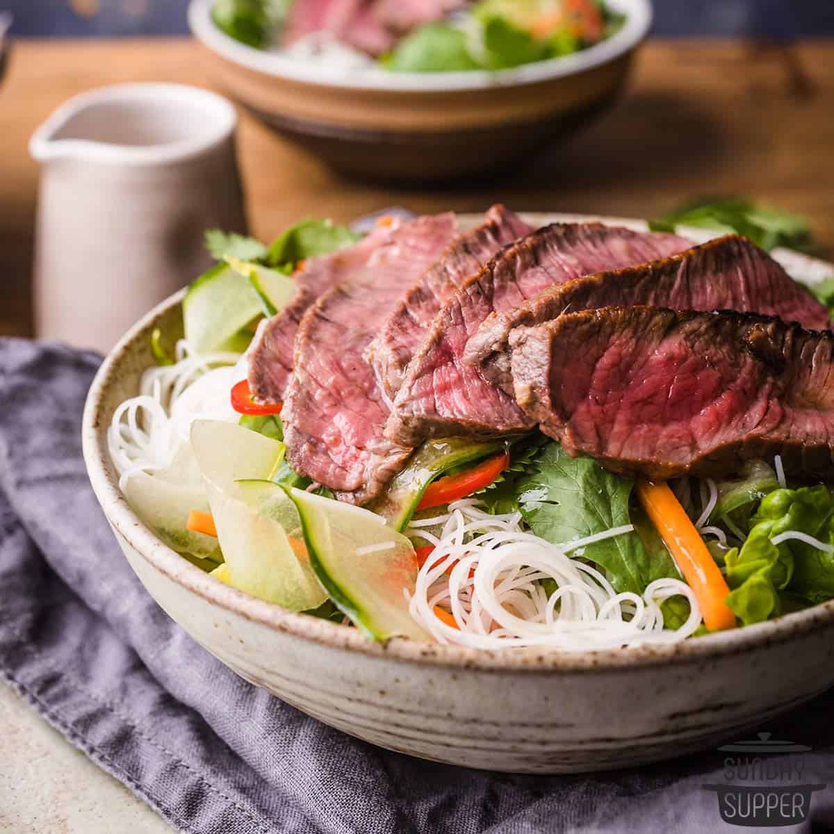 Slices of sirloin steak over rice noodles and vegetables