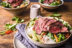 Sirloin steak sliced thinly over rice noodles and crisp veggies in a bowl