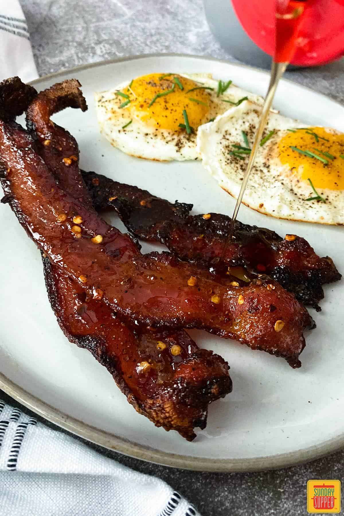 air fryer candied bacon on a plate with two eggs