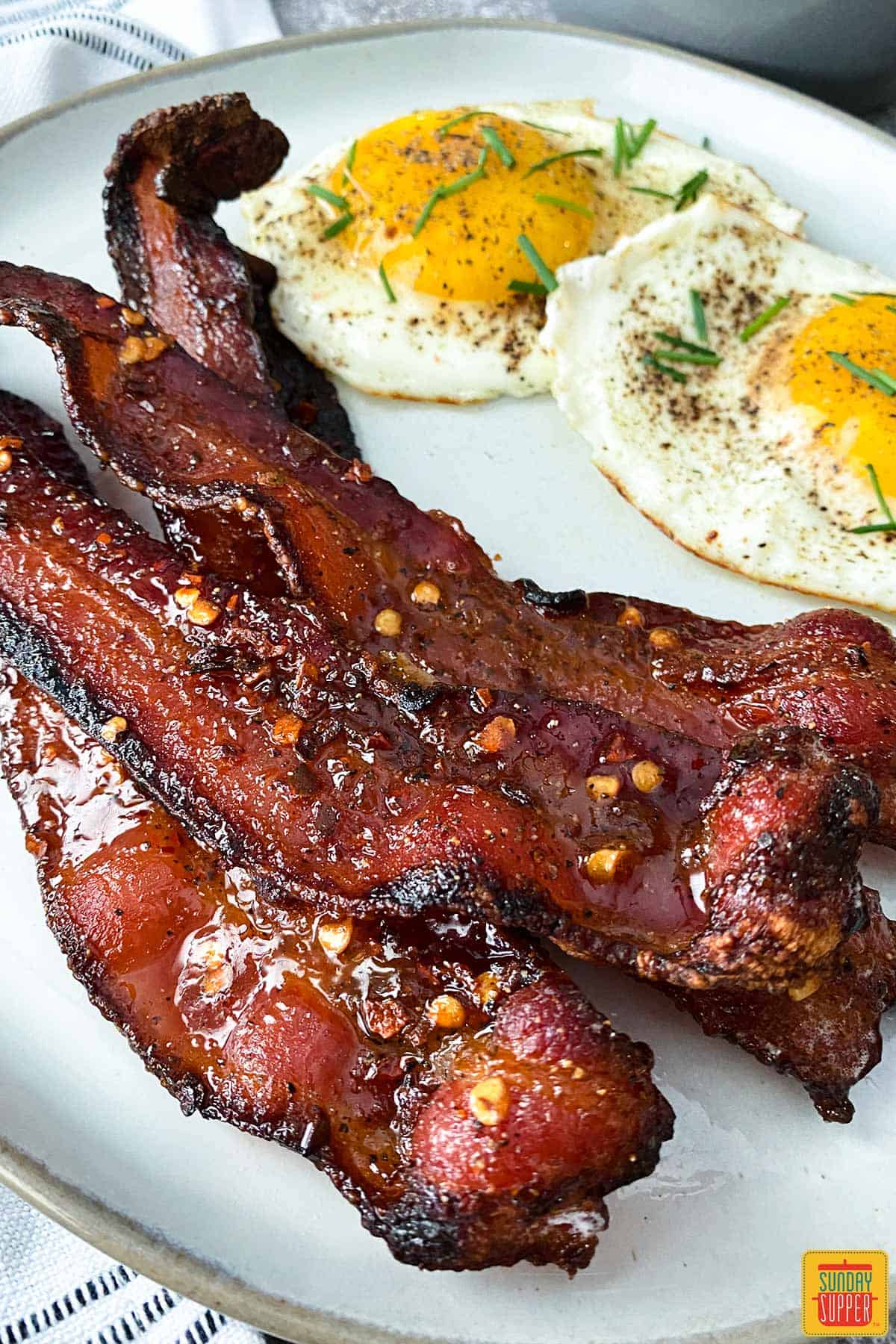four strips of candied bacon on a plate with two eggs