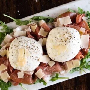 Burrata cheese topped with parmesan on a bed of prosciutto and arugula with olive oil