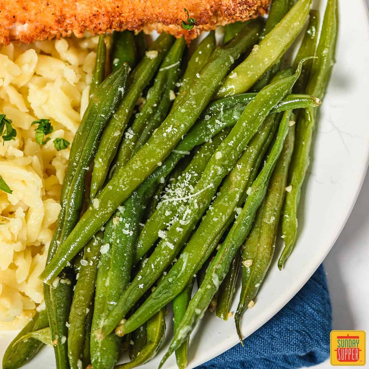 Instant pot green beans on a white plate with cheesy orzo and air fried pork chops