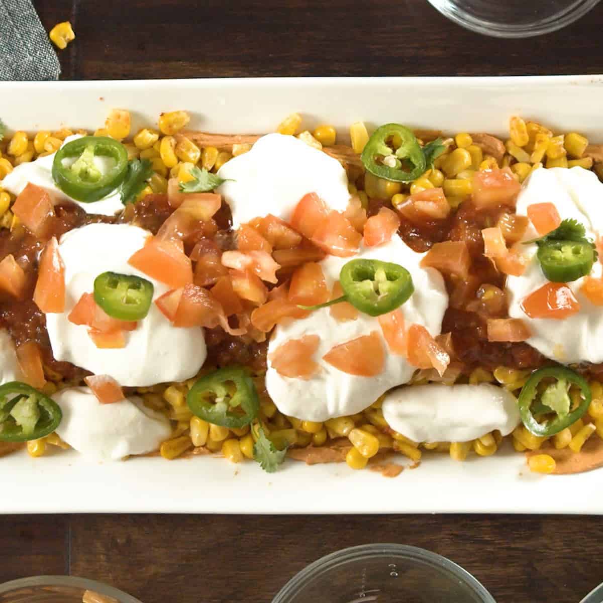 Taco dip on a white plate with tomatoes and jalapenos on top