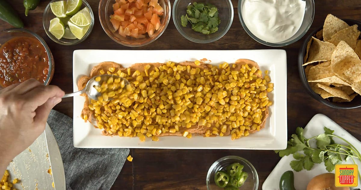 Corn layered over taco dip on a white dish