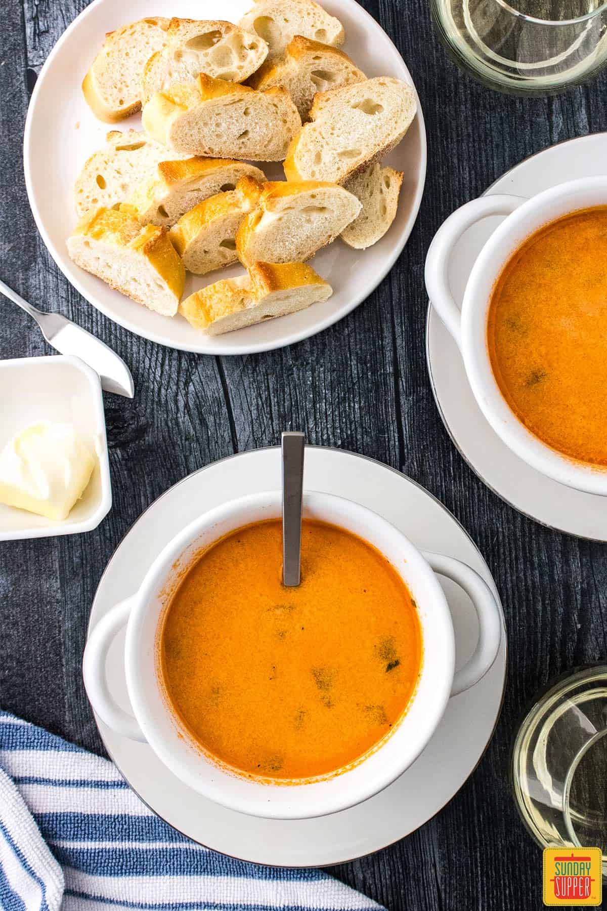 shrimp bisque in two white bowls with french bread slices on a plate