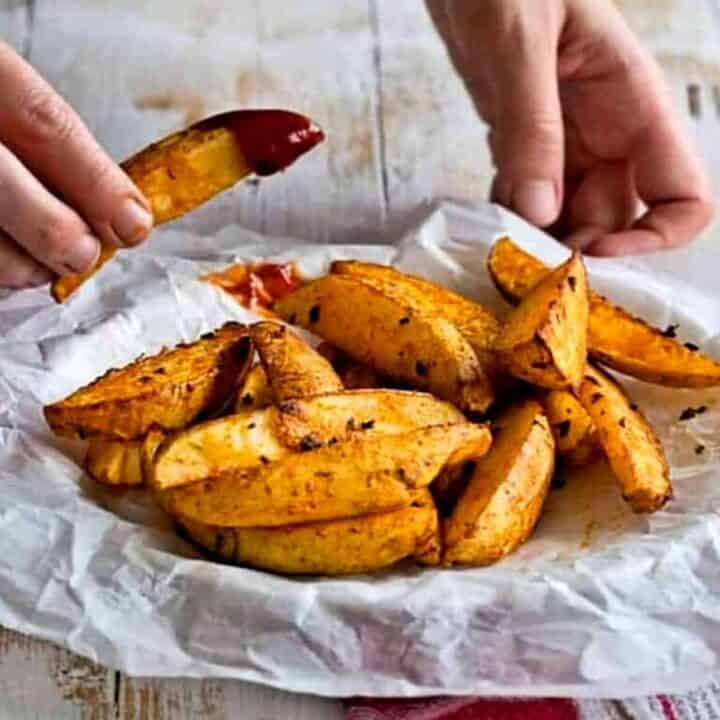 Crispy baked potato wedges on parchment paper dipped in ketchup