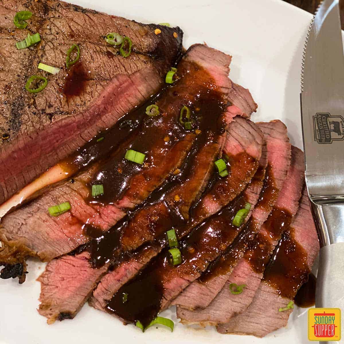 grilled london broil with sauce and a knife