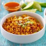 Mexican street corn casserole in a white dish up close with hot sauce in a bowl behind it