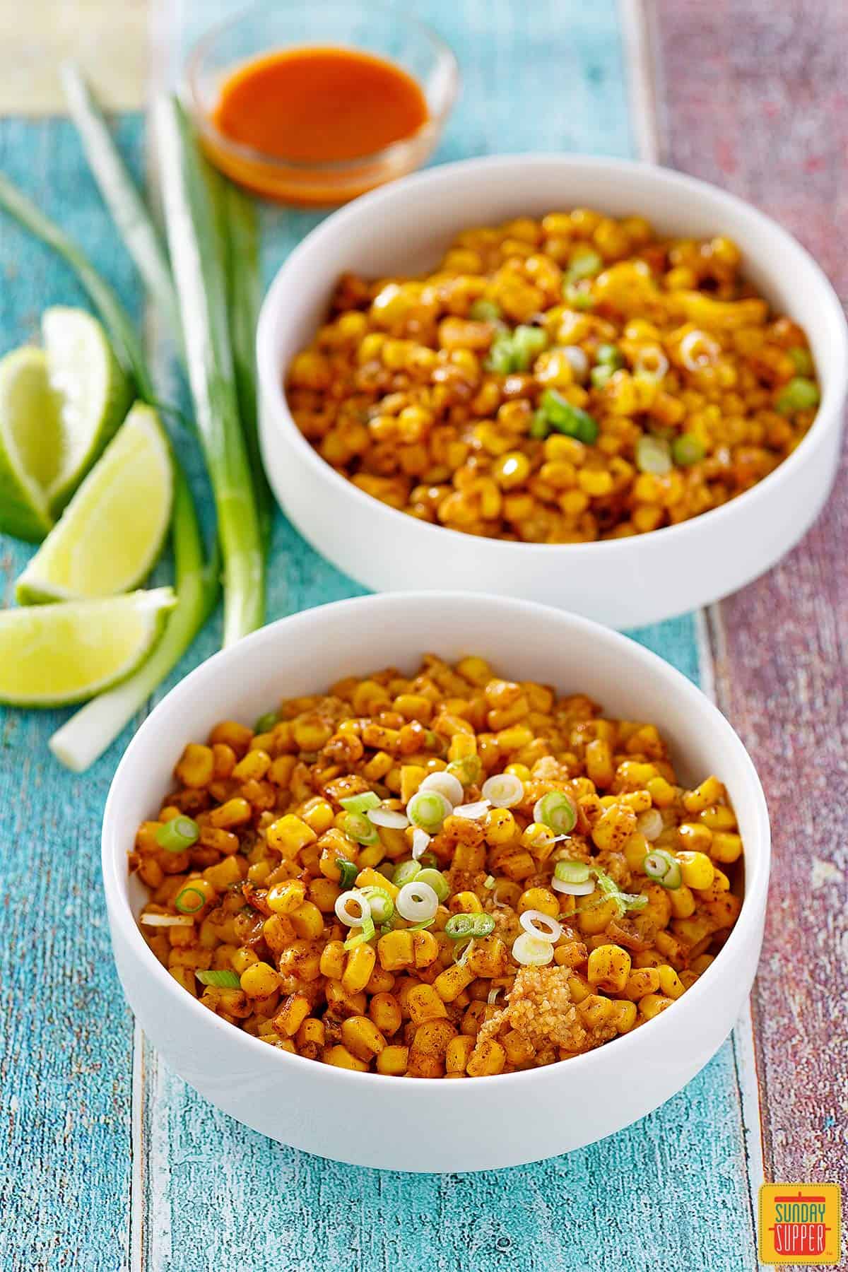 Two bowls of Mexican street corn casserole with lime wedges