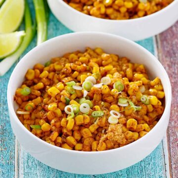 Mexican street corn casserole in two white bowls with slices of limes