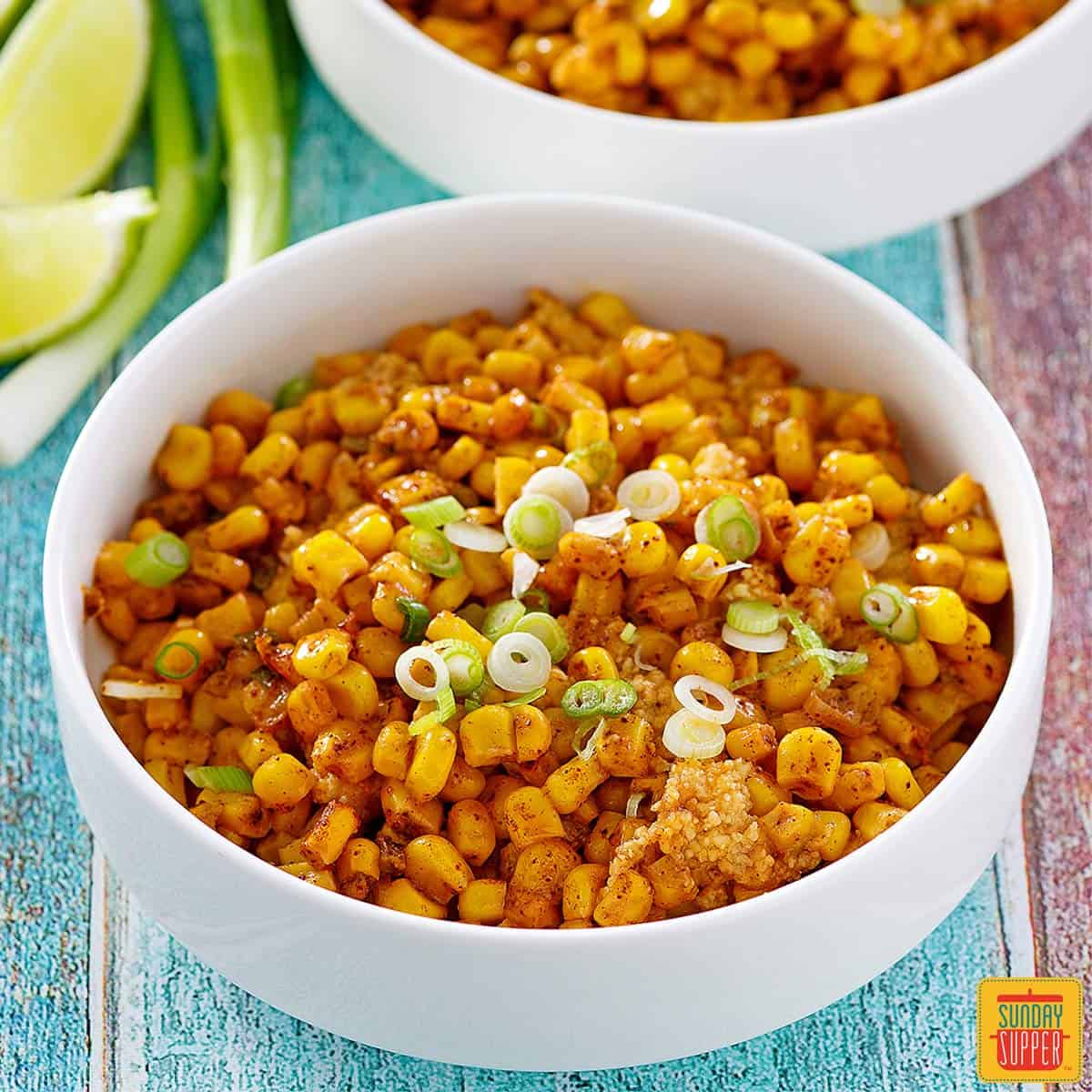 Mexican street corn casserole in two white bowls with slices of limes