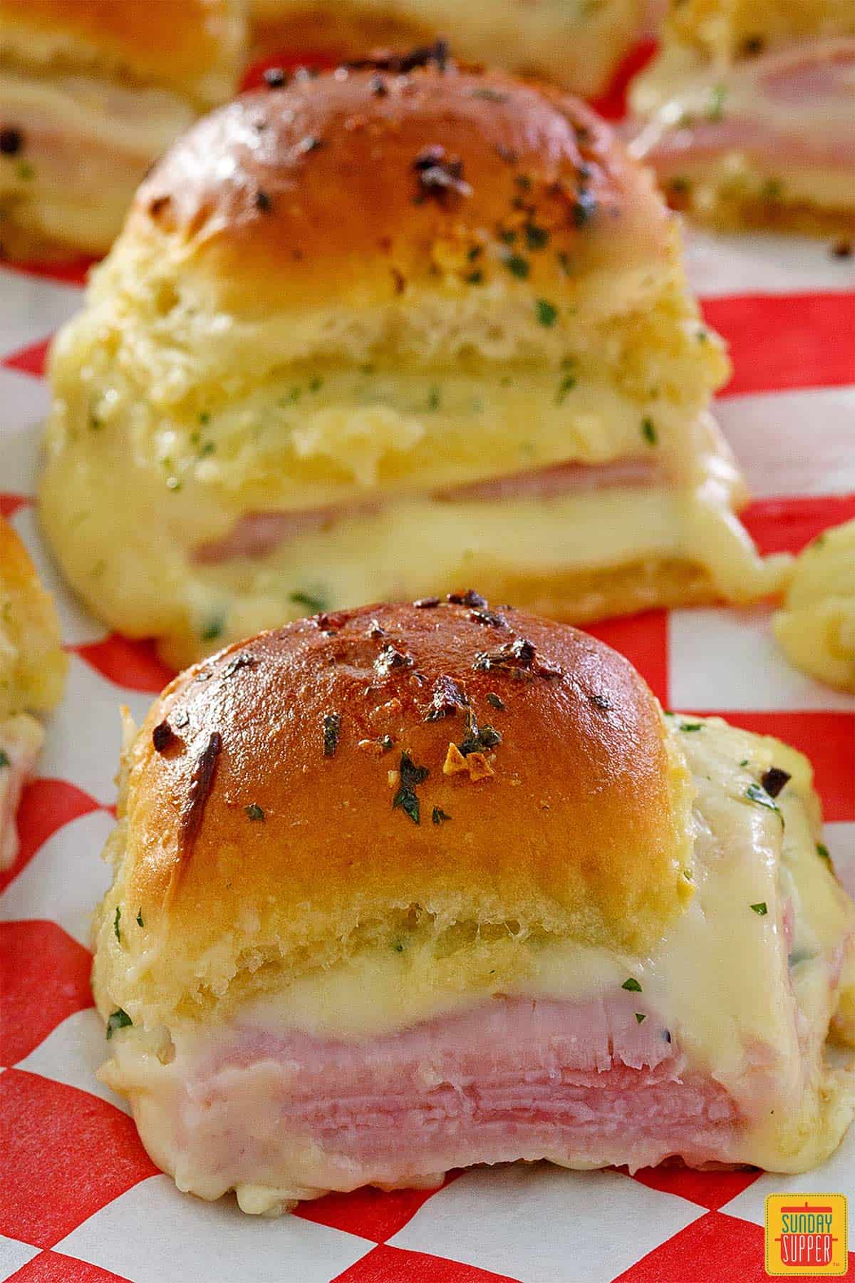 Two ham and cheese sliders on red and white checked paper