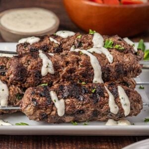 Lebanese beef kafta on a plate with garlic cream sauce drizzled on top