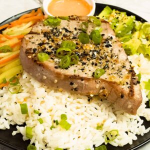 Grilled tuna steak on a bed of rice with vegetables and spicy mayo