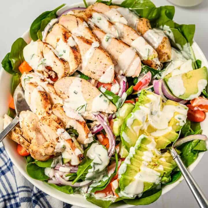Slices of grilled chicken on a salad with buttermilk ranch dressing and a fork