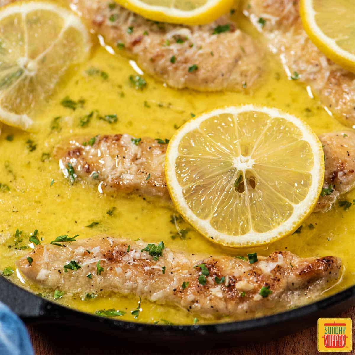 Lemon butter chicken in skillet with sauce and lemon slices