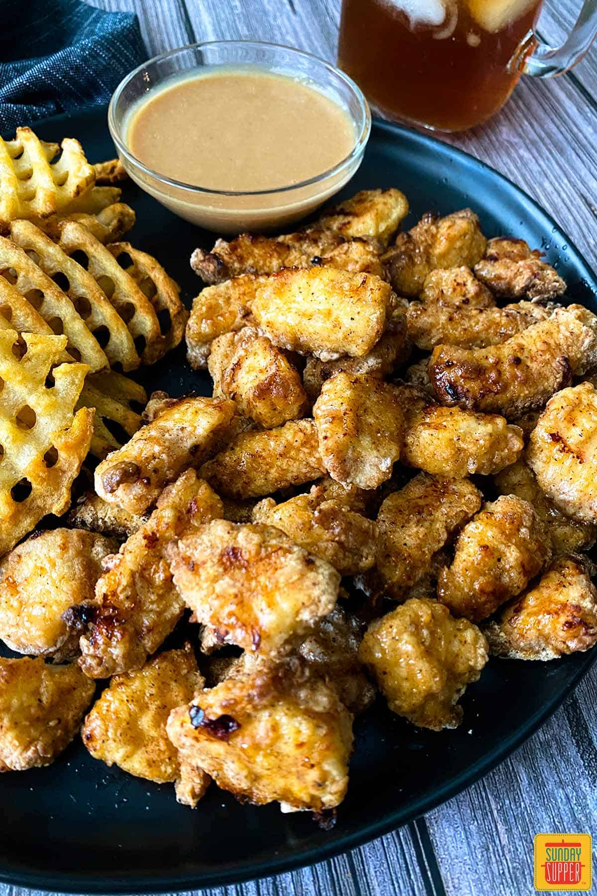 Up close air fryer chick-fil-a nuggets on a black plate with waffle fries and chick-fil-a sauce in a cup