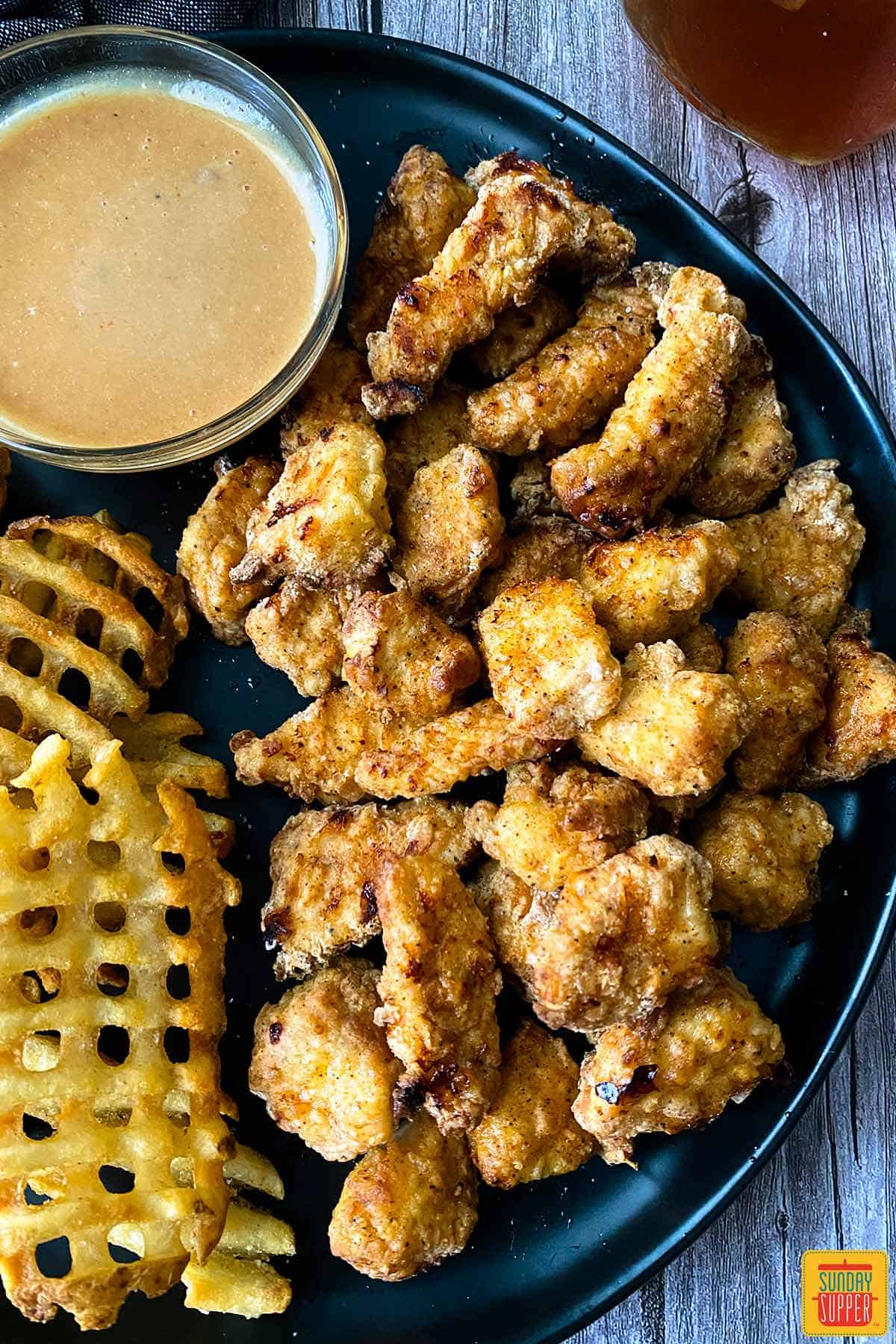 Air fryer chicken nuggets on a plate with chick-fil-a sauce and waffle fries