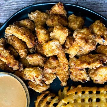 Chick-fil-a nuggets on black plate with chick-fil-a sauce and waffle fries