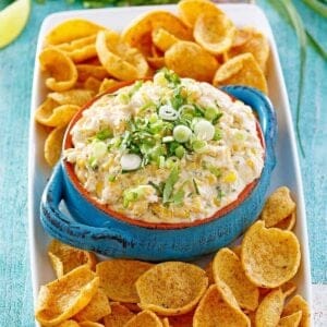 Street corn dip in a blue bowl with corn chips and green onions