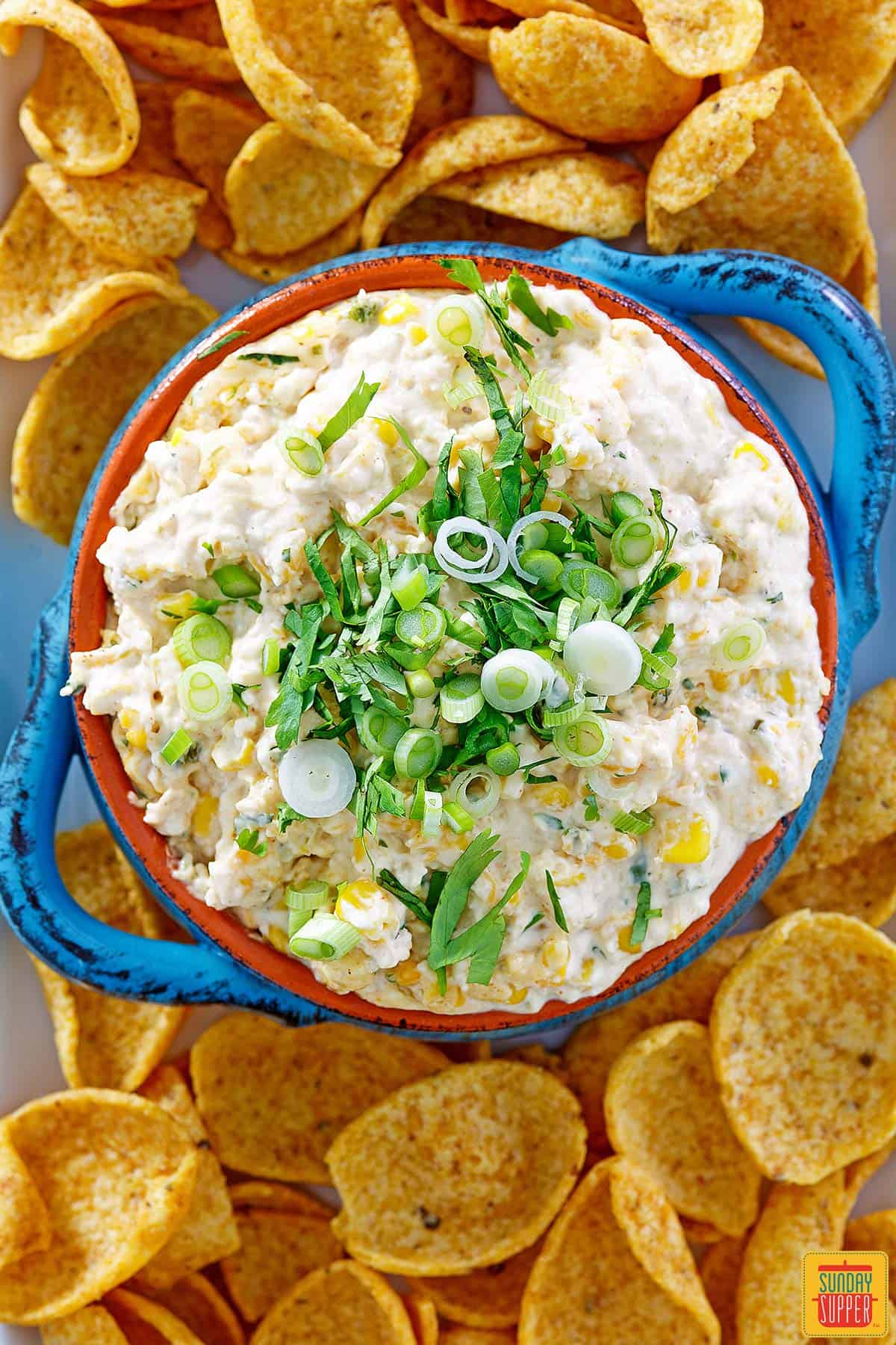 Top-down view of street corn dip in a blue bowl with green onions on top