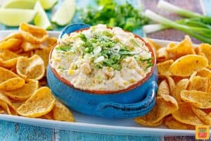 Street corn dip in a blue bowl with corn chips and green onions on top