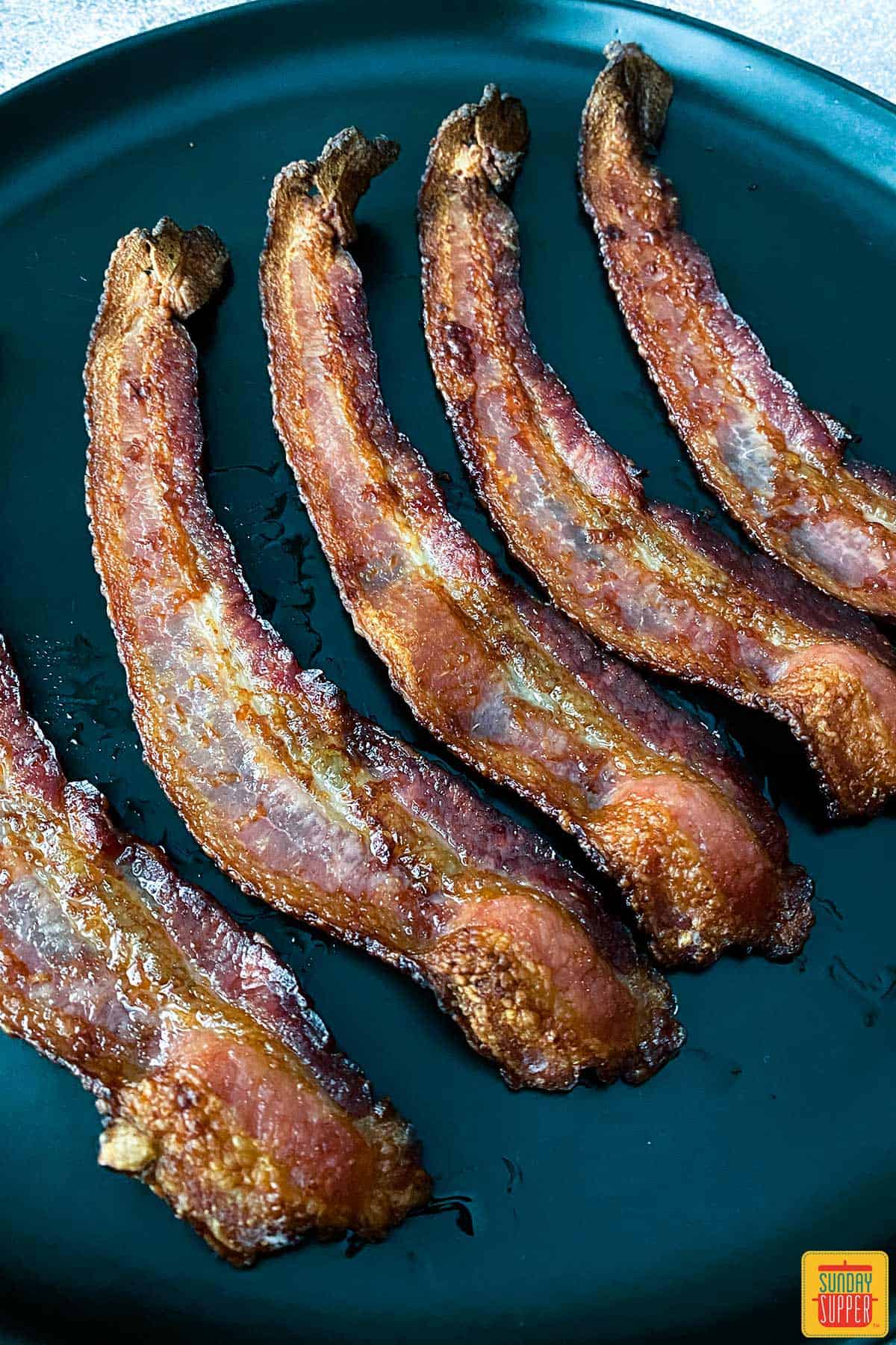 Strips of air fried bacon on a black plate