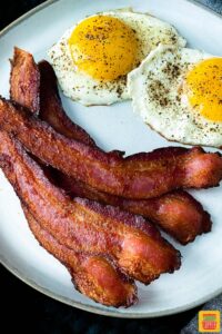 Strips of bacon on a white plate with two eggs