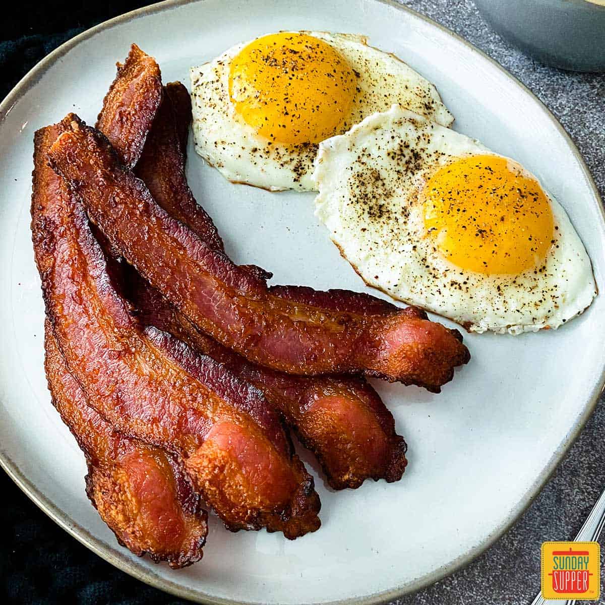 Air fryer bacon on a white plate with two sunny side up eggs