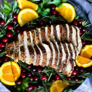 Air fryer turkey breast on a platter with greens, citrus, and cranberries, sliced