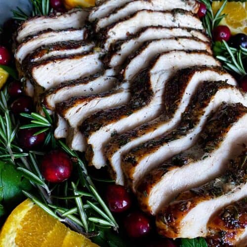 close up slices of air fryer turkey breast with cranberries, greens, and citrus slices