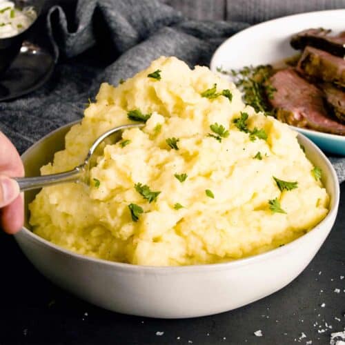 creamy mashed potatoes piled high in a white dish with a spoon and chives