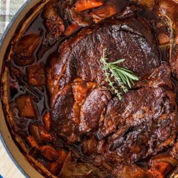 Chuck roast cooked in a pot with broth and vegetables.