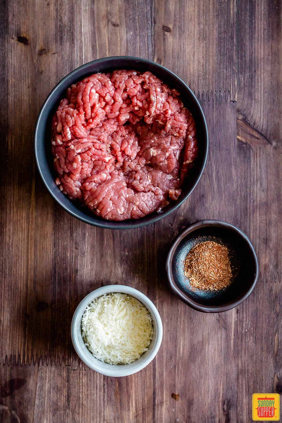 Burger meat with seasoning and parmesan in separate bowls