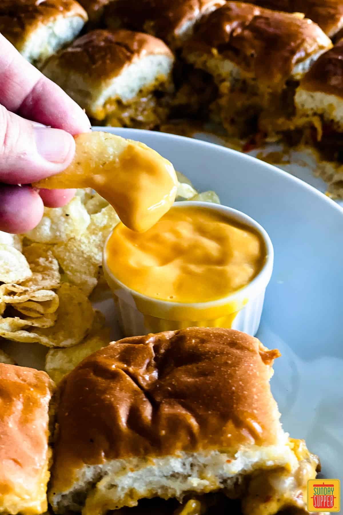 Dipping a chip into Ragu double cheddar cheese sauce on a white plate with sliders