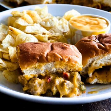 Two philly cheesesteak sliders on a plate with potato chips and cheese dip to the side