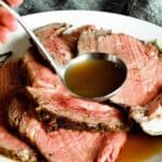 pouring au jus from a ladle over a roast