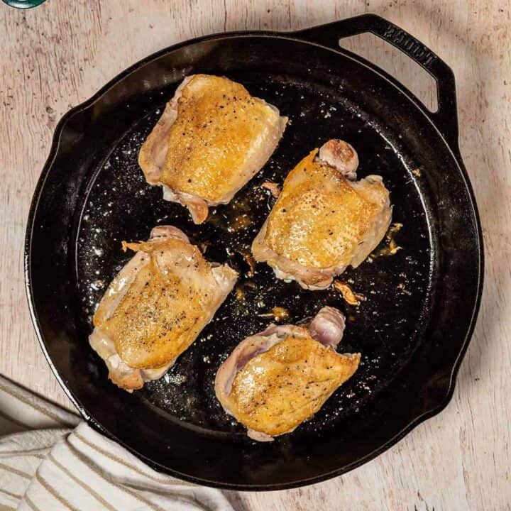 Four chicken thighs cooking in a pan