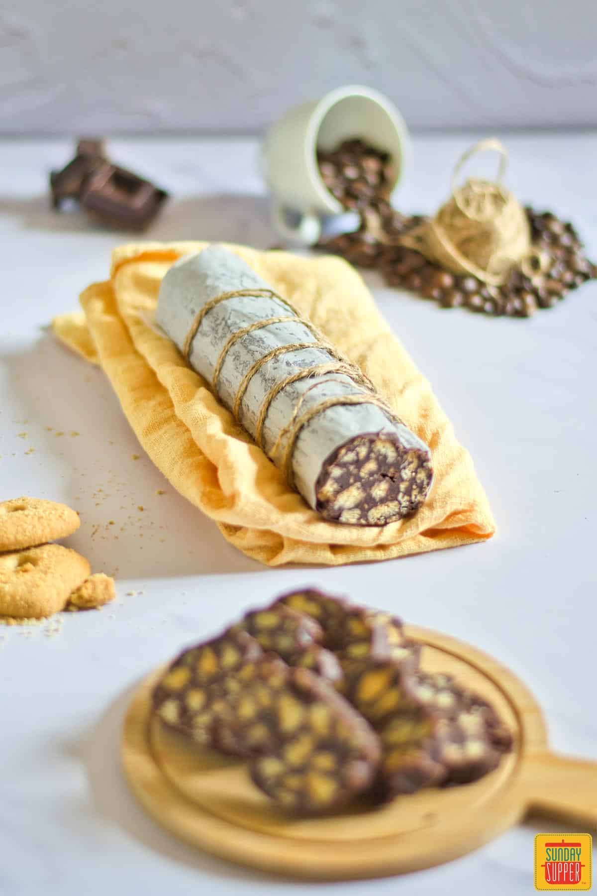 Portuguese chocolate salami on a yellow cloth with some sliced on a board