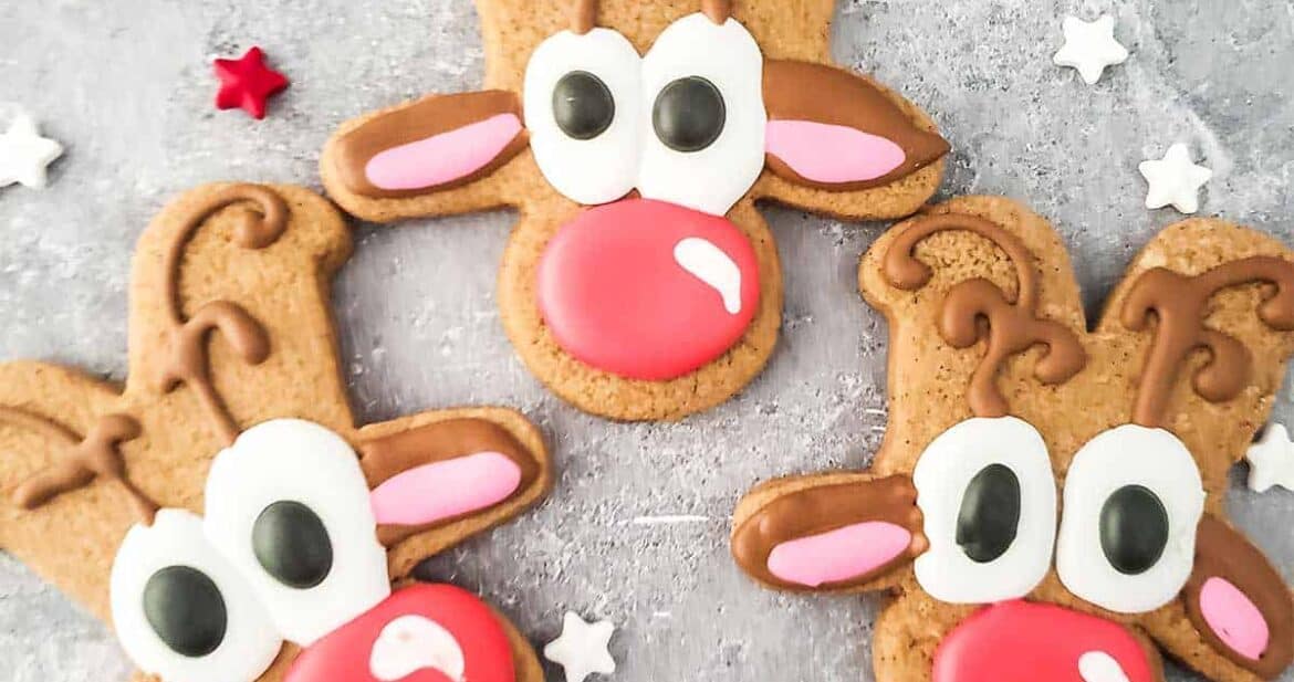 Three reindeer cookies on a surface with star sprinkles