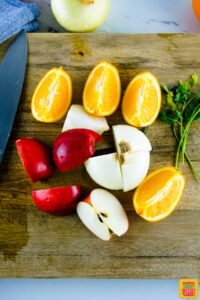 Apples, oranges, and onions on a cutting board with fresh herbs