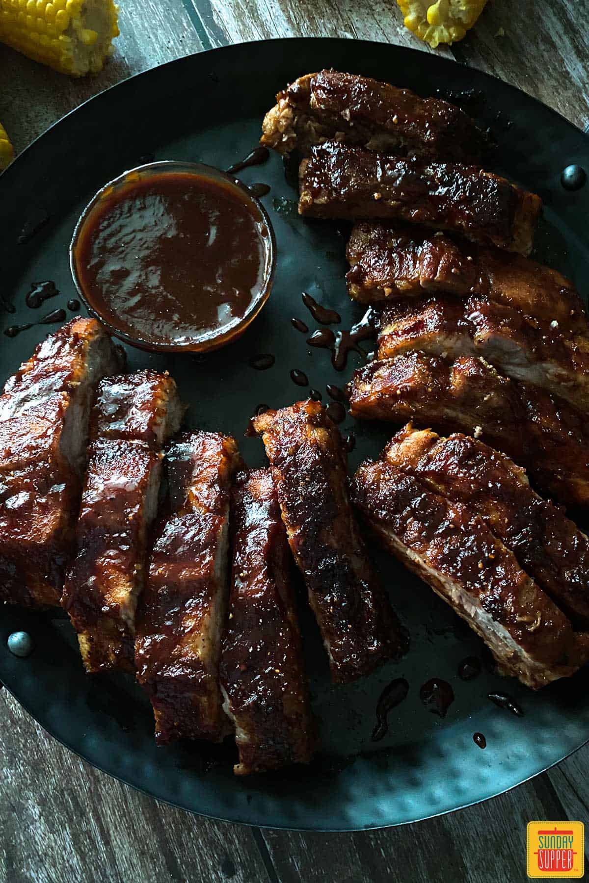 Air fryer Baby back ribs on a black plate with bbq sauce in a bowl